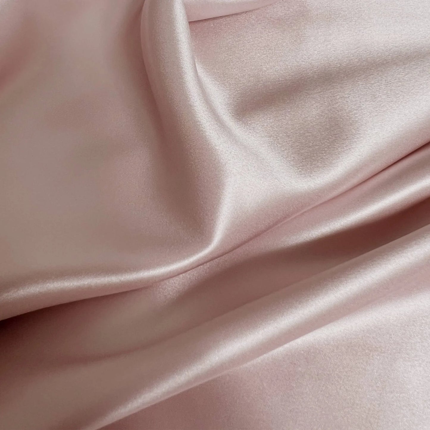 Close-up of smooth, light pink mulberry silk fabric with folds.