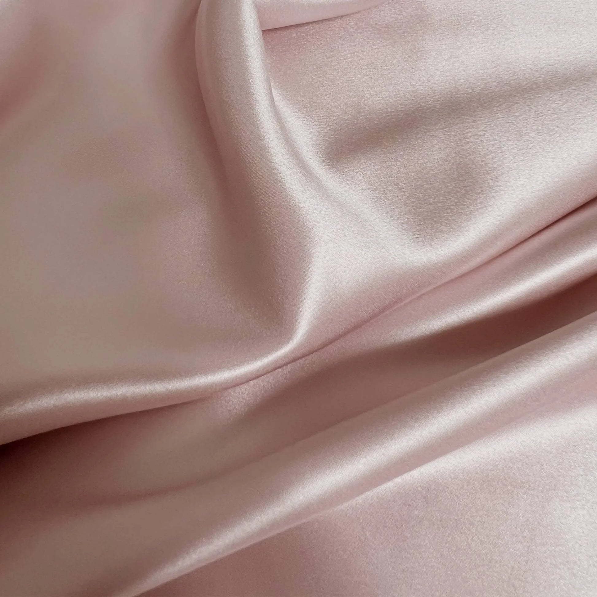 Close-up of smooth, light pink mulberry silk fabric with folds.
