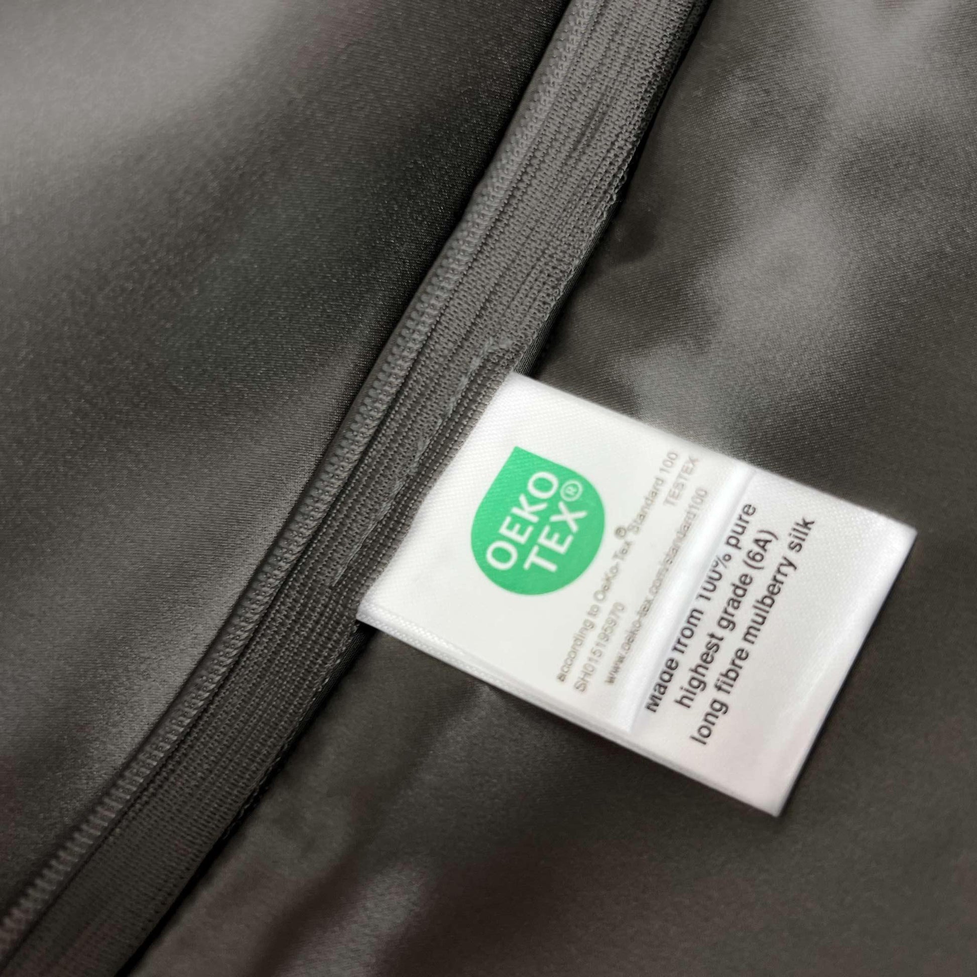 OEKO-TEX label on a dark grey silk fabric background
